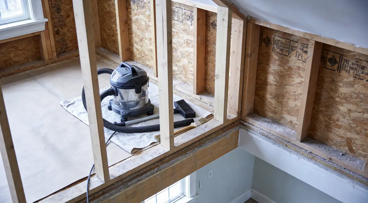 HEPA vacuum and brushes beside a partly cleaned framing bay