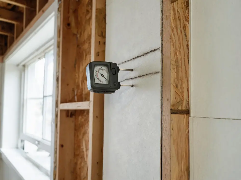 Moisture meter pressed against drywall beside a water stain