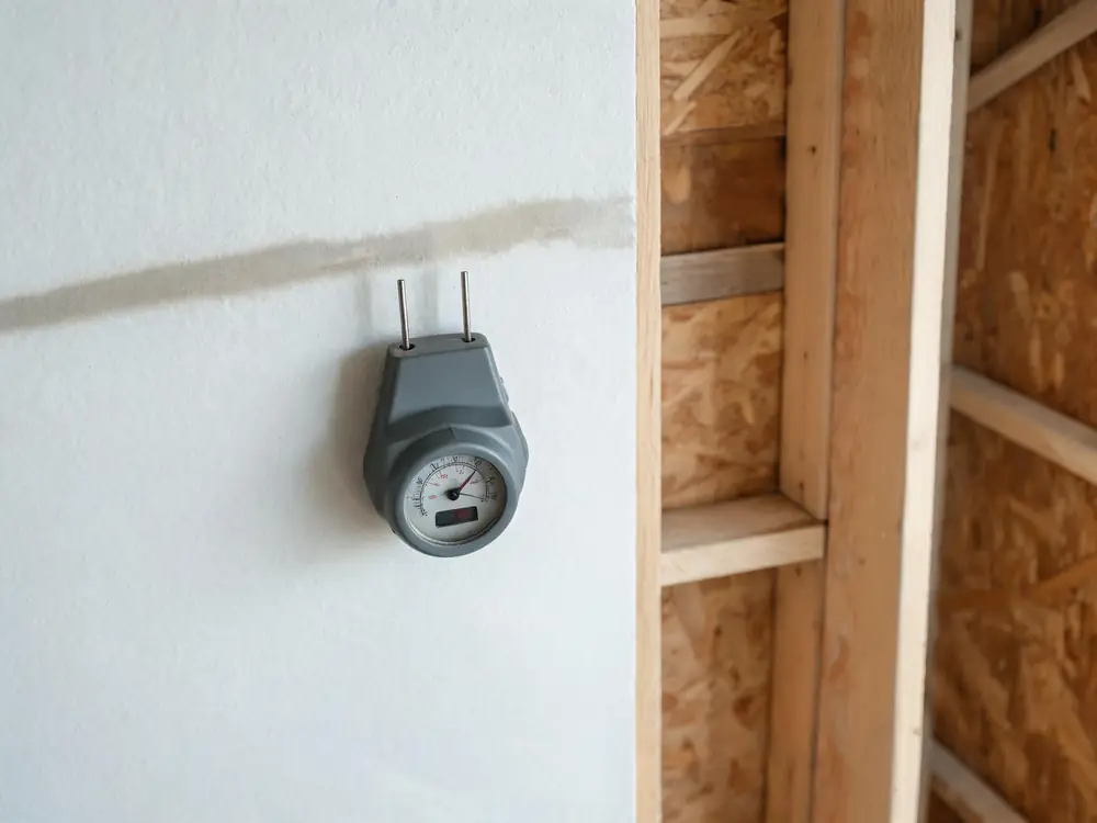 Moisture meter pressed against drywall beside a water stain