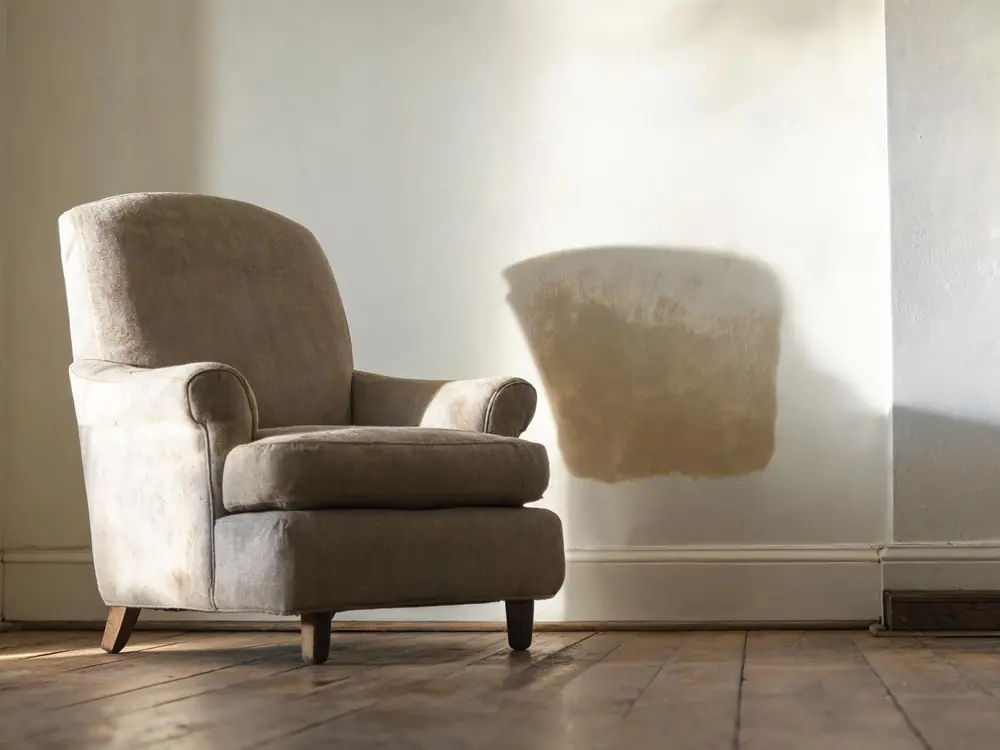 Armchair pulled away from a damp wall showing marks behind